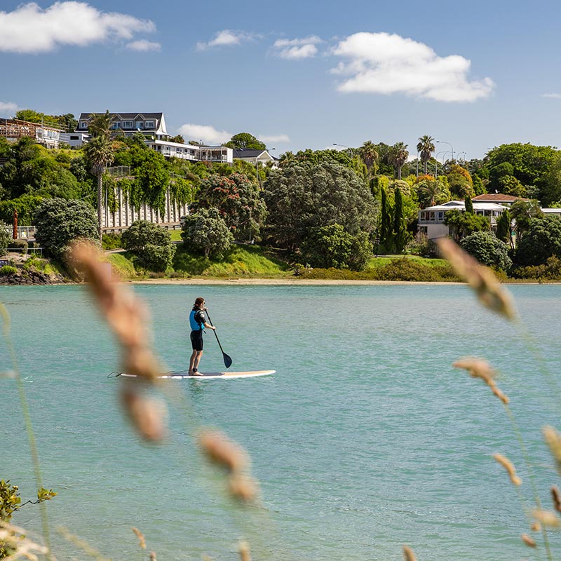 Paddleboarder on calm blue water in Orewa.